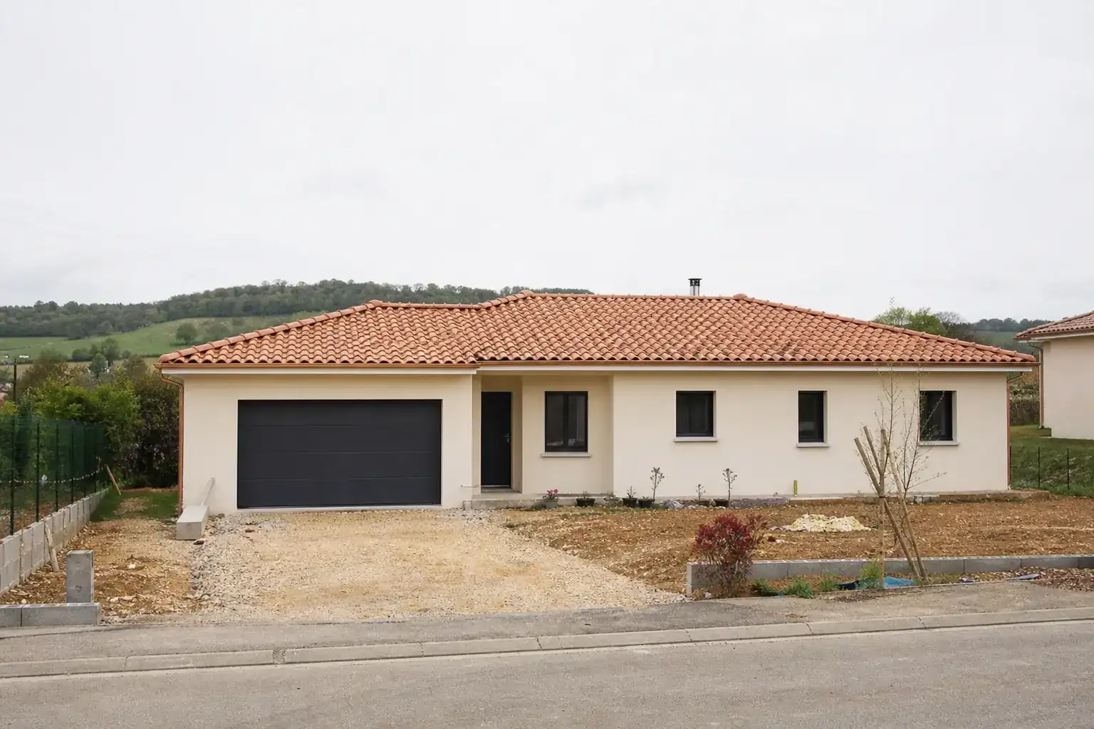 Maison de plain-pied en enduit clair et tuiles terre cuite, vue de face depuis la rue