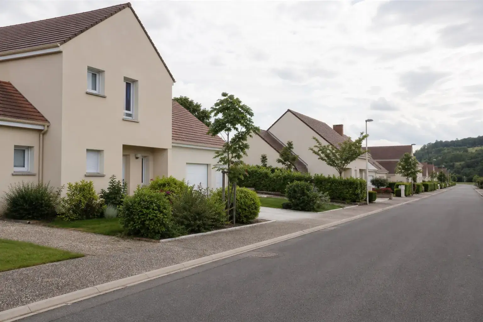 Rue résidentielle bordée de maisons individuelles récentes aux façades enduites claires, murets bas et stationnement en bordure de chaussée
