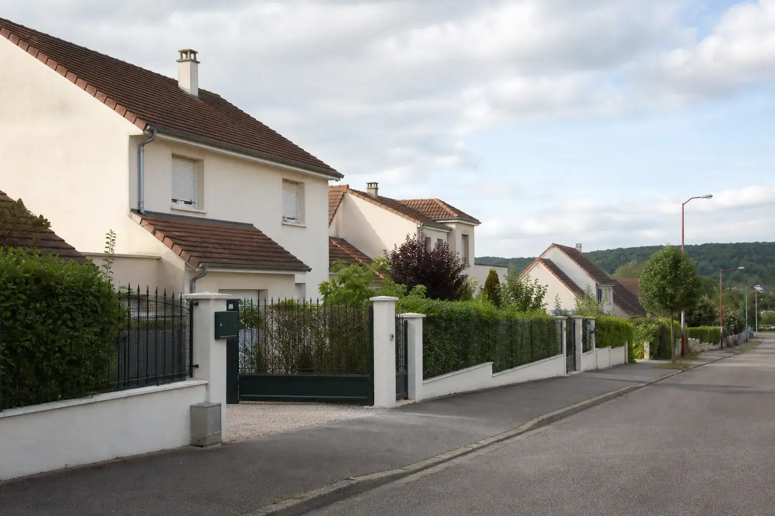 Rue résidentielle bordée de maisons individuelles récentes aux façades enduites claires, trottoirs et haies basses