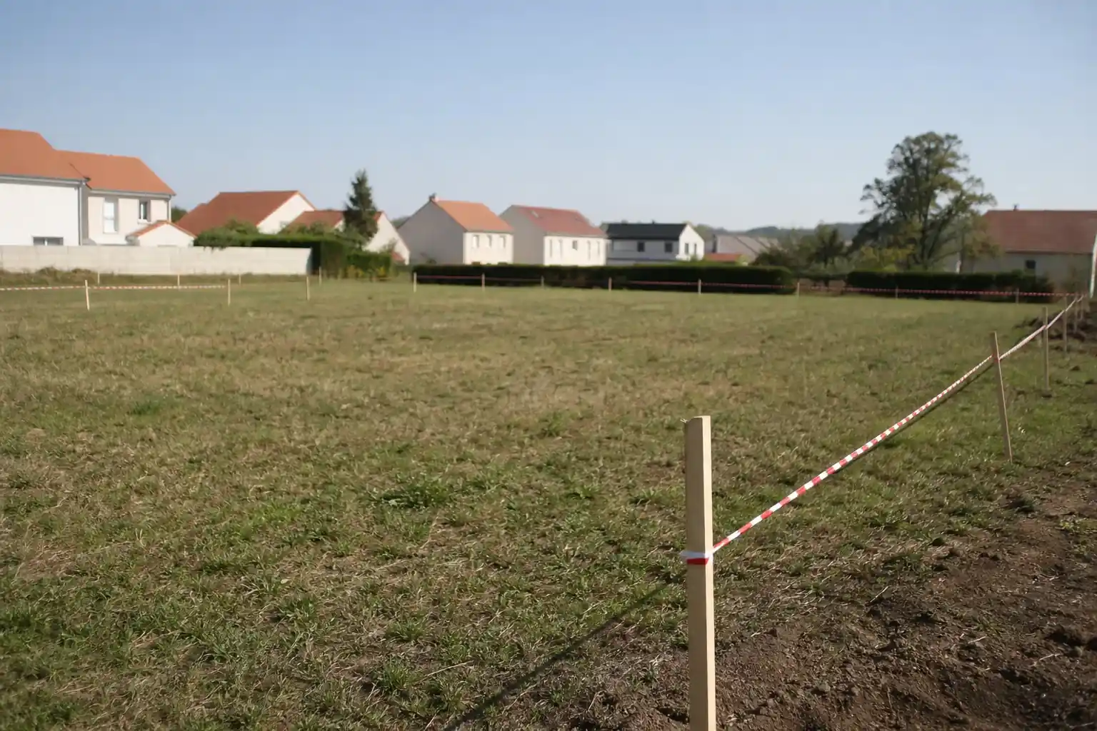 Terrain à bâtir borné en périphérie d’une commune, piquets et rubans de chantier